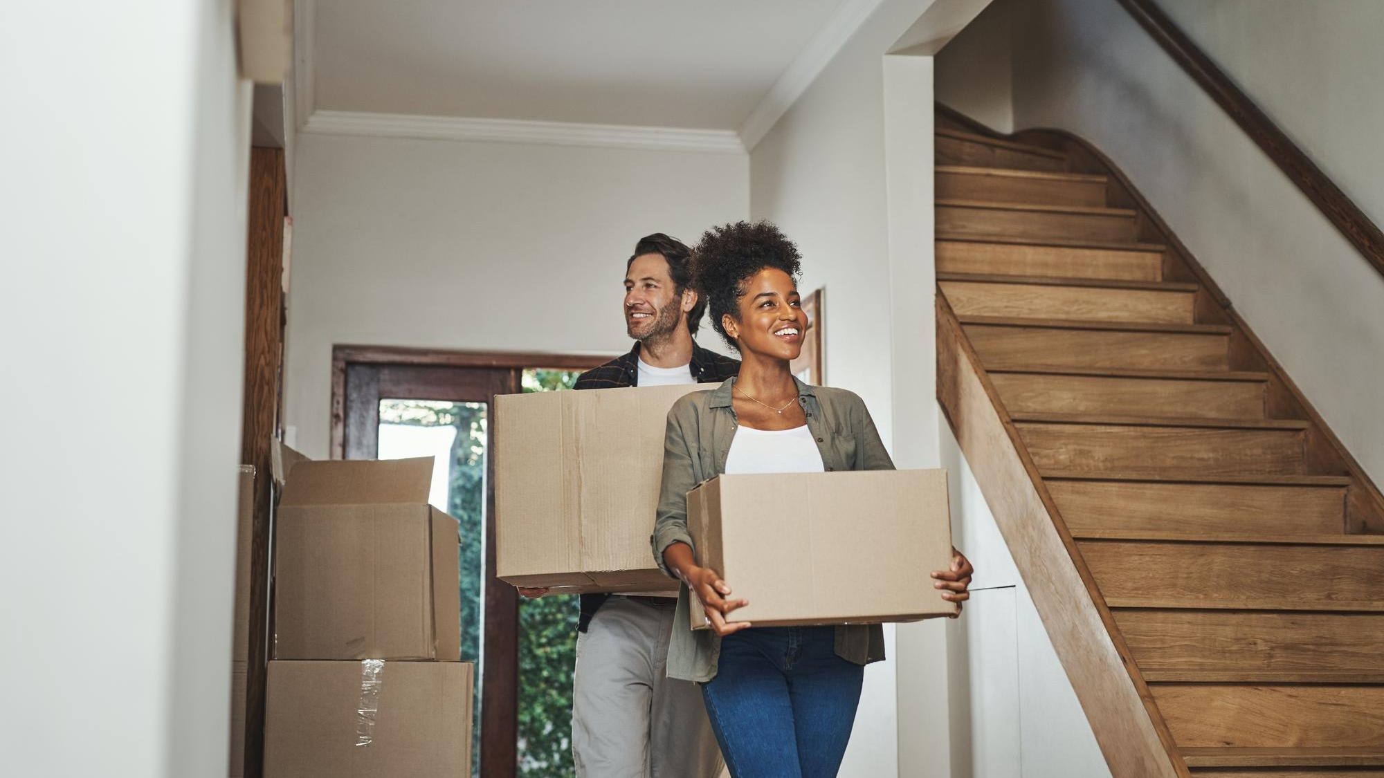 Excited happy and young couple moving into a new home together while carrying and packing household boxes Smiling positive and cheerful husband and wife in a lovely modern real estate property