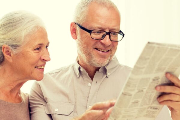 family, holidays, age and people concept - happy senior couple reading newspaper at home
