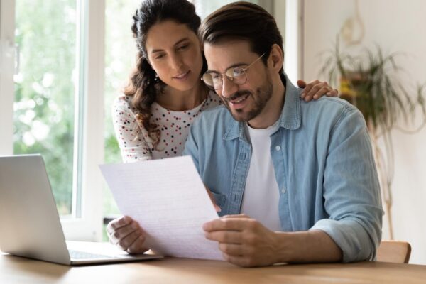 Happy affectionate young family couple reading paper correspondence with good news feeling curious of getting interested information Smiling bonding man and woman getting bank notification letter