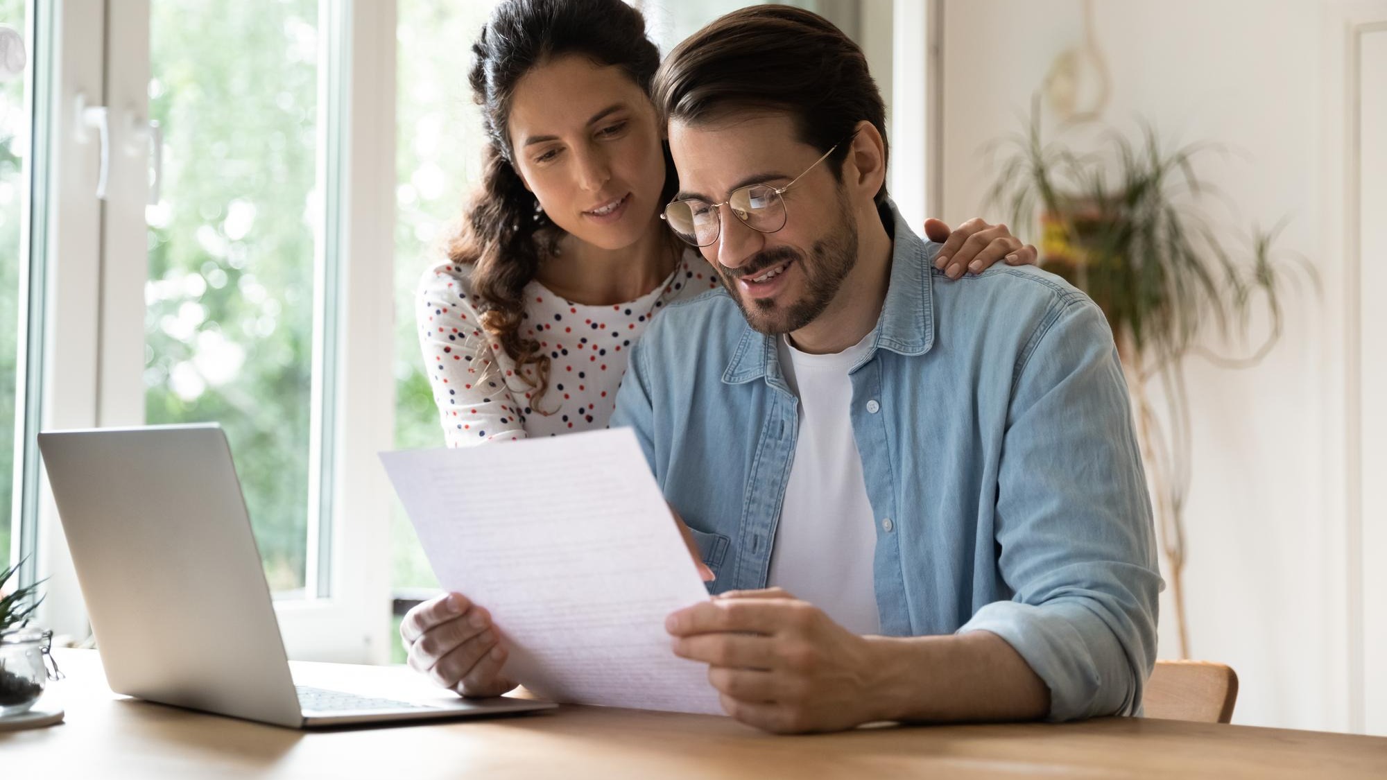 Happy affectionate young family couple reading paper correspondence with good news feeling curious of getting interested information Smiling bonding man and woman getting bank notification letter