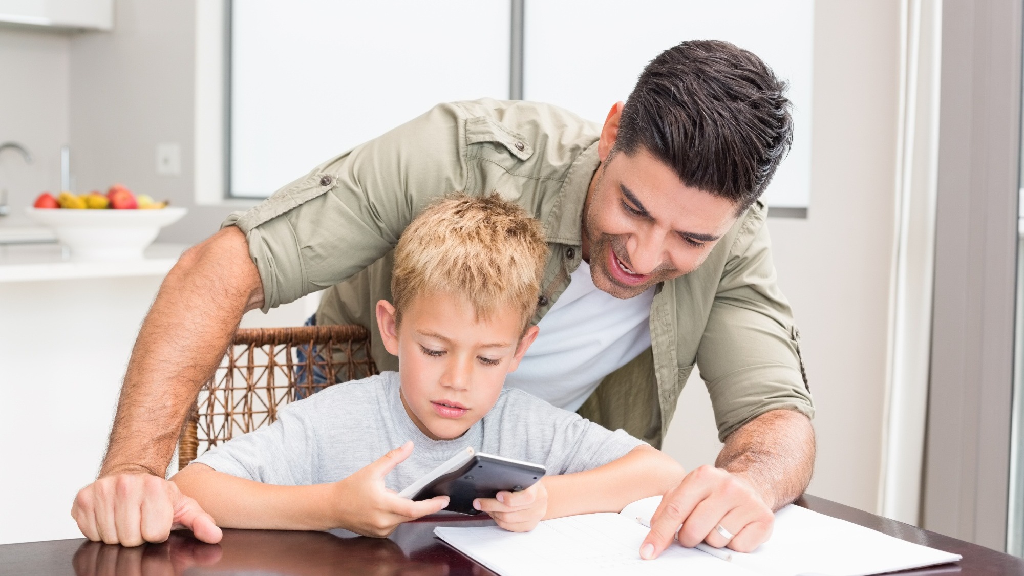Smiling father helping son with math homework at table