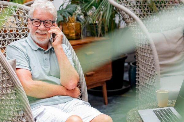 White haired senior man sitting on armchair talking on mobile phone enjoying tech and social