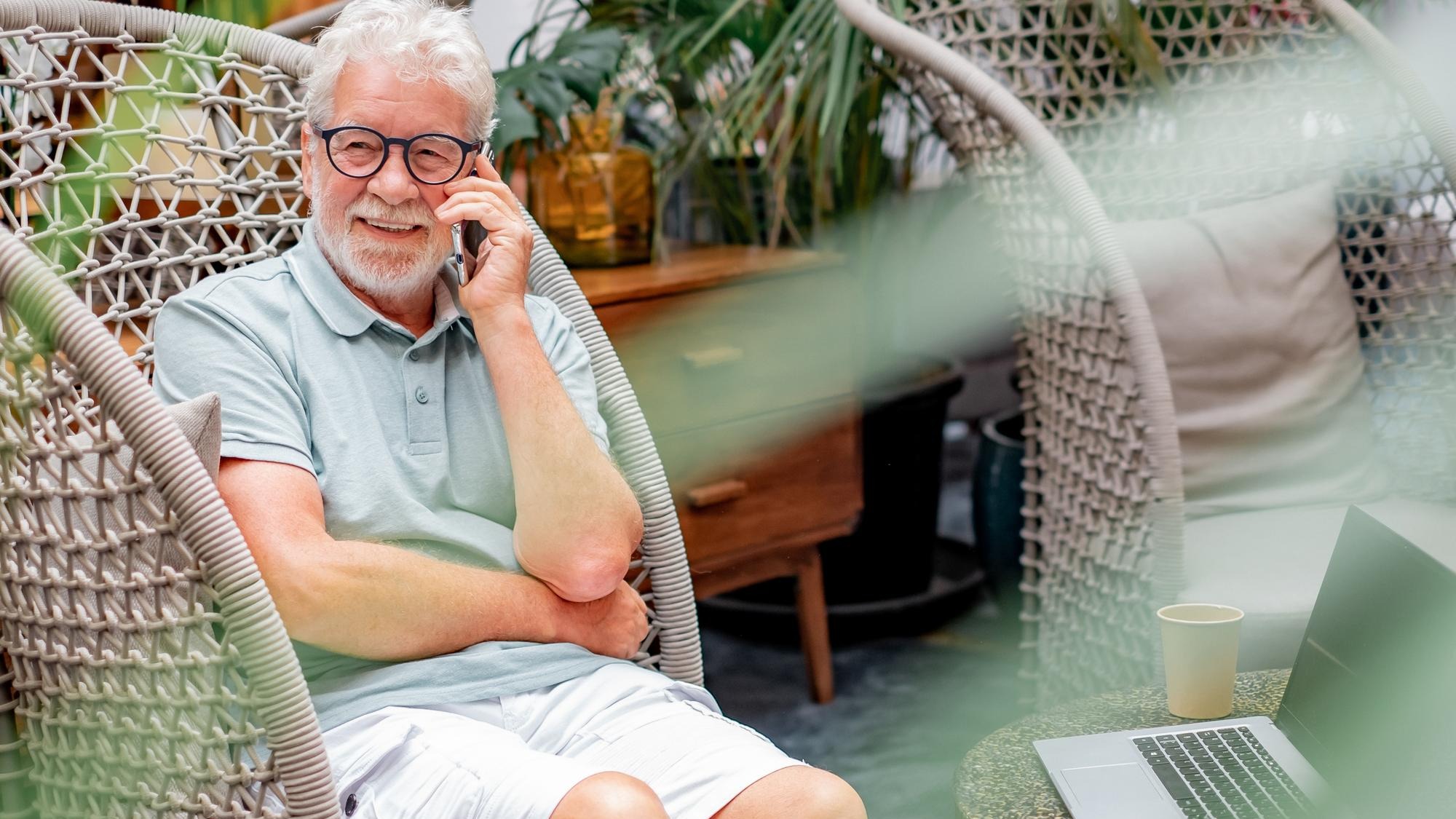 White haired senior man sitting on armchair talking on mobile phone enjoying tech and social