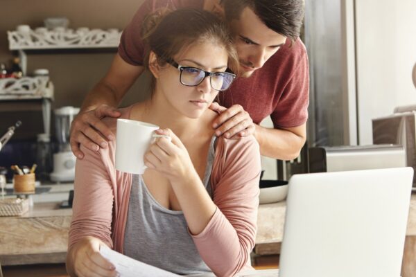 Frustrated young husband and wife doing paperwork together, calculating their expenses, managing bills, using laptop computer and calculator in modern kitchen
