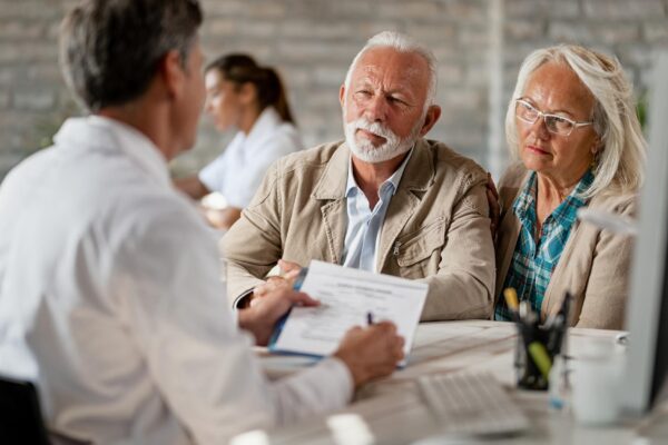 Senior couple consulting with healthcare worker about their insurance policy while having a meeting at clinic