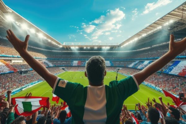 A man is watching a soccer game in a stadium with his arms in the air aig