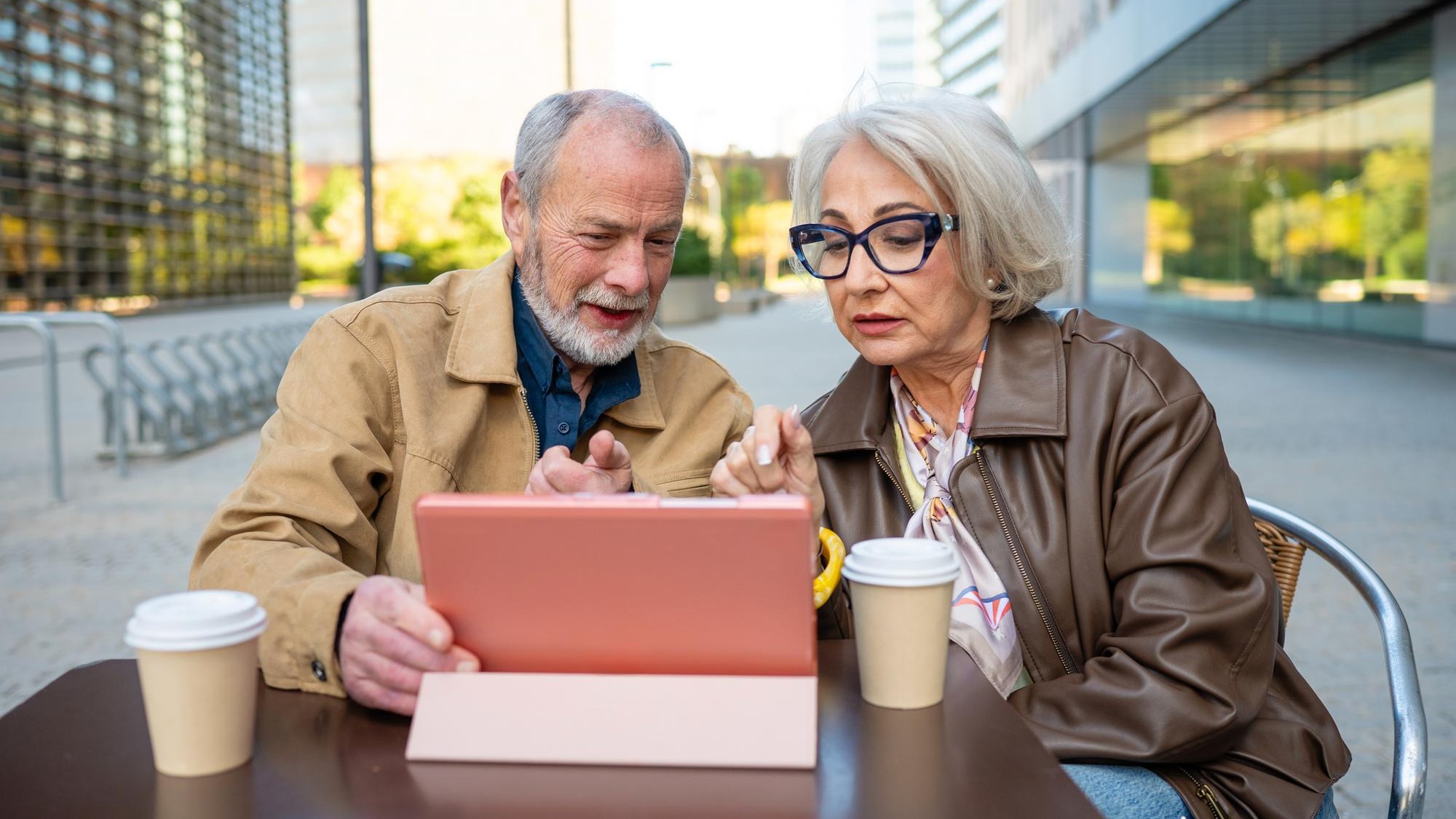 Focused senior companions sharing content on a digital tablet at a cafe