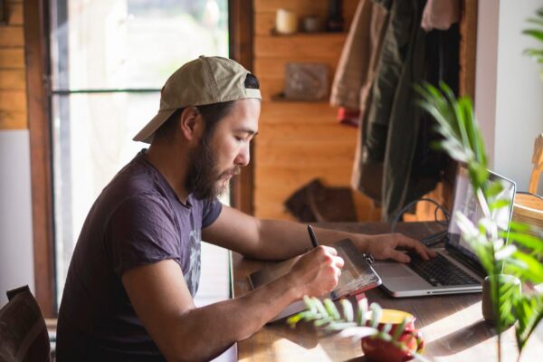 Asian man with beard working on a tablet and a laptop at home