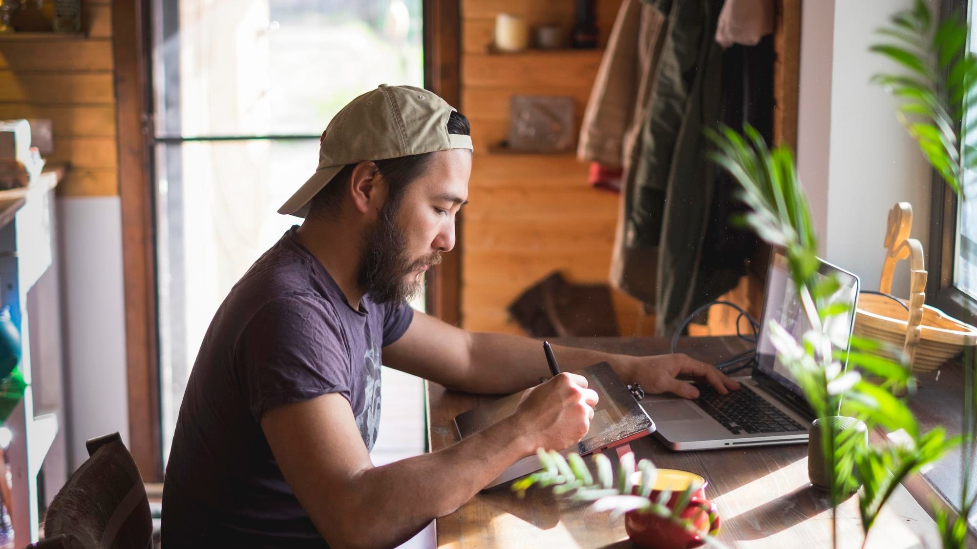 Asian man with beard working on a tablet and a laptop at home