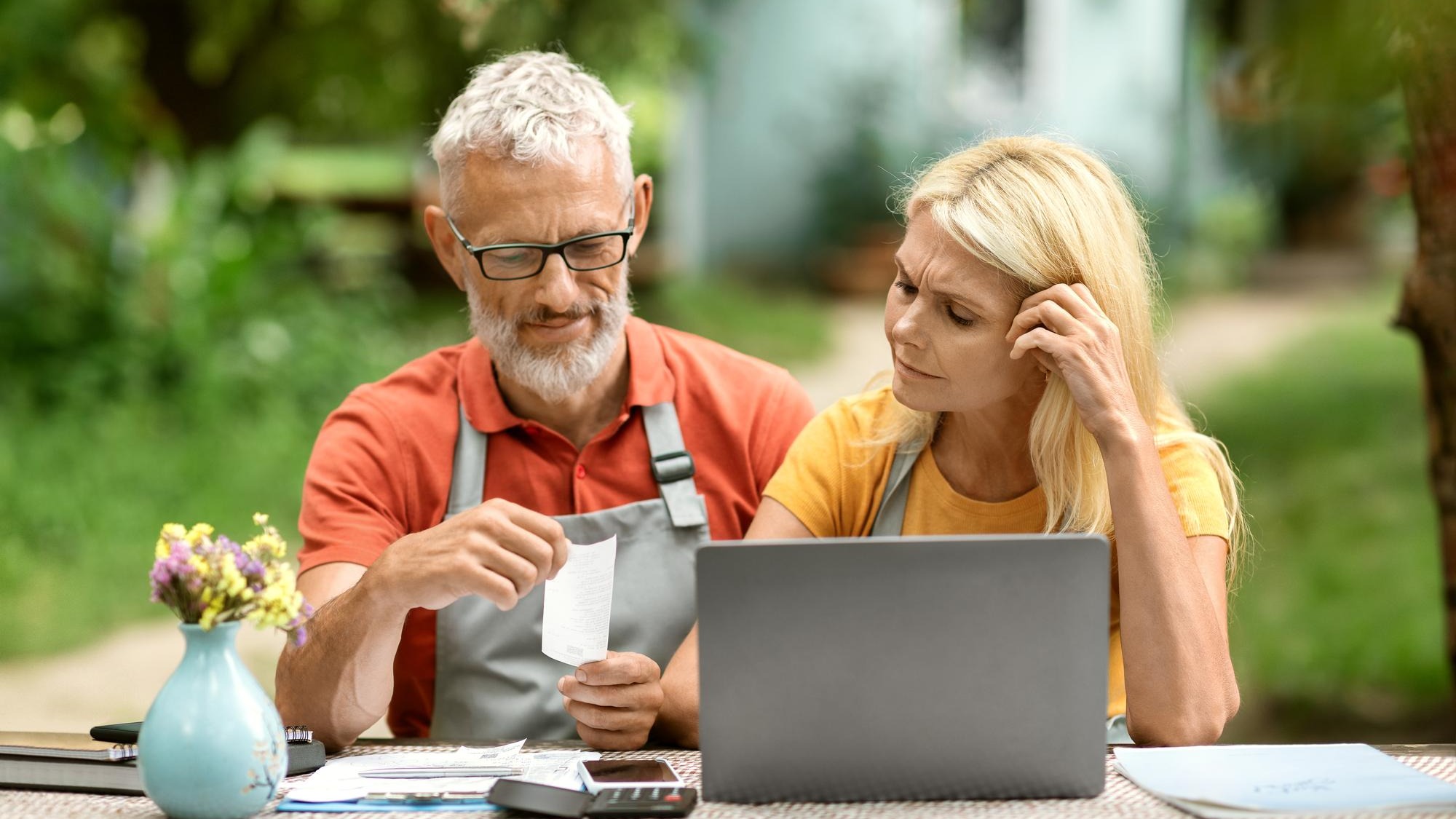 Stressed senior couple with laptop checking bills sitting at table in garden