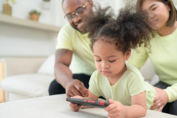 Little children play and learn things in the wide world on tablet with parents to supervise and help in the living room of the house on vacation