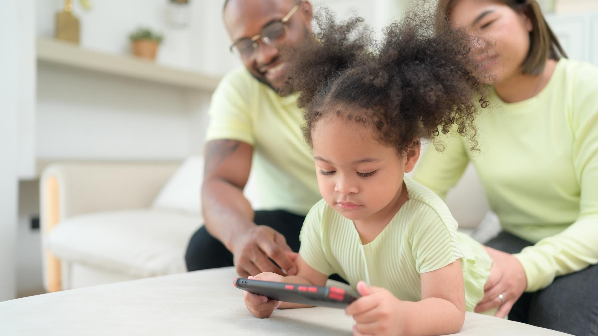 Little children play and learn things in the wide world on tablet with parents to supervise and help in the living room of the house on vacation