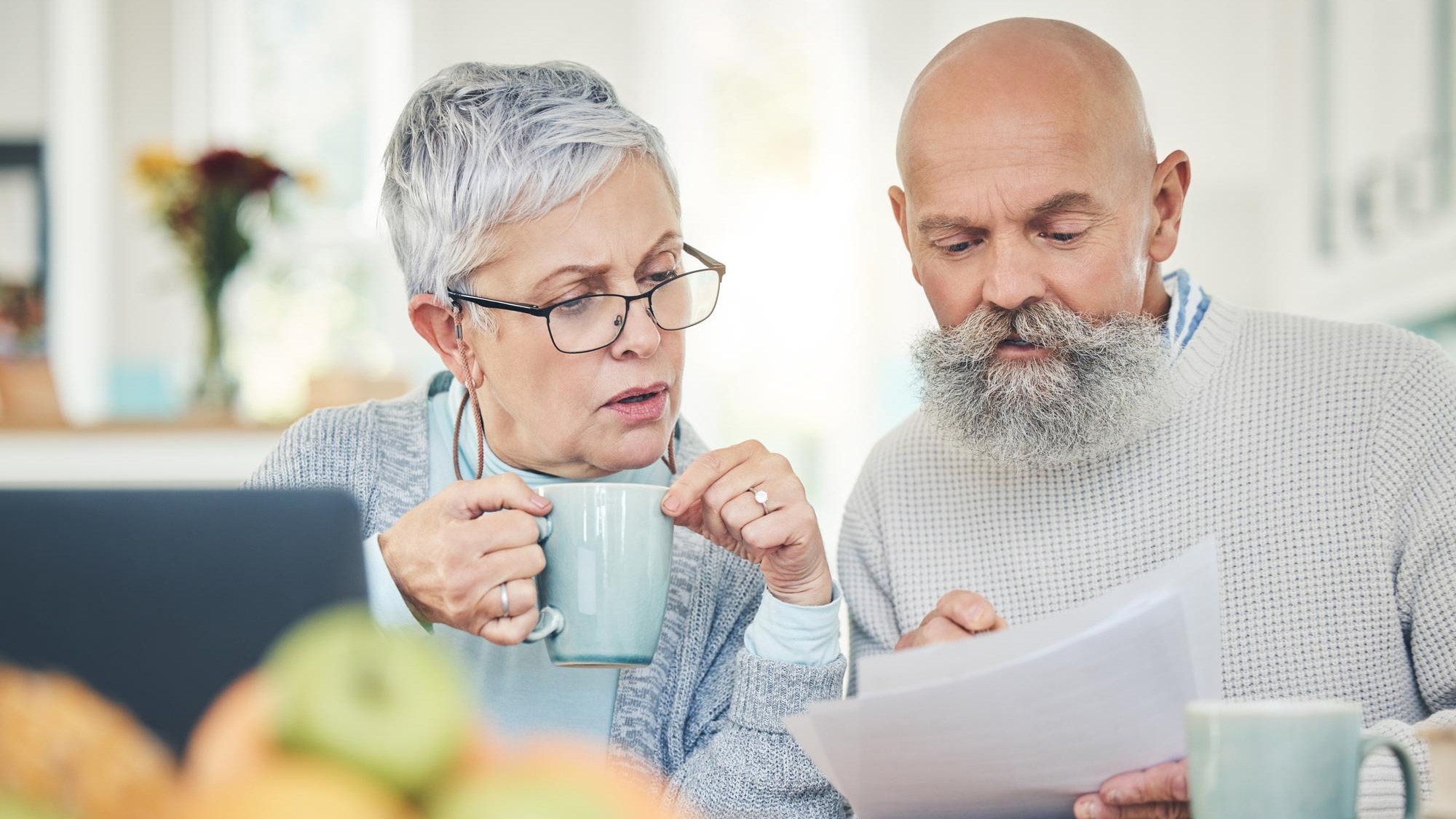 Laptop senior couple and finance documents in home for budget savings or taxes in house Computer retirement and man and woman with paperwork for financial planning insurance or bills with coffee