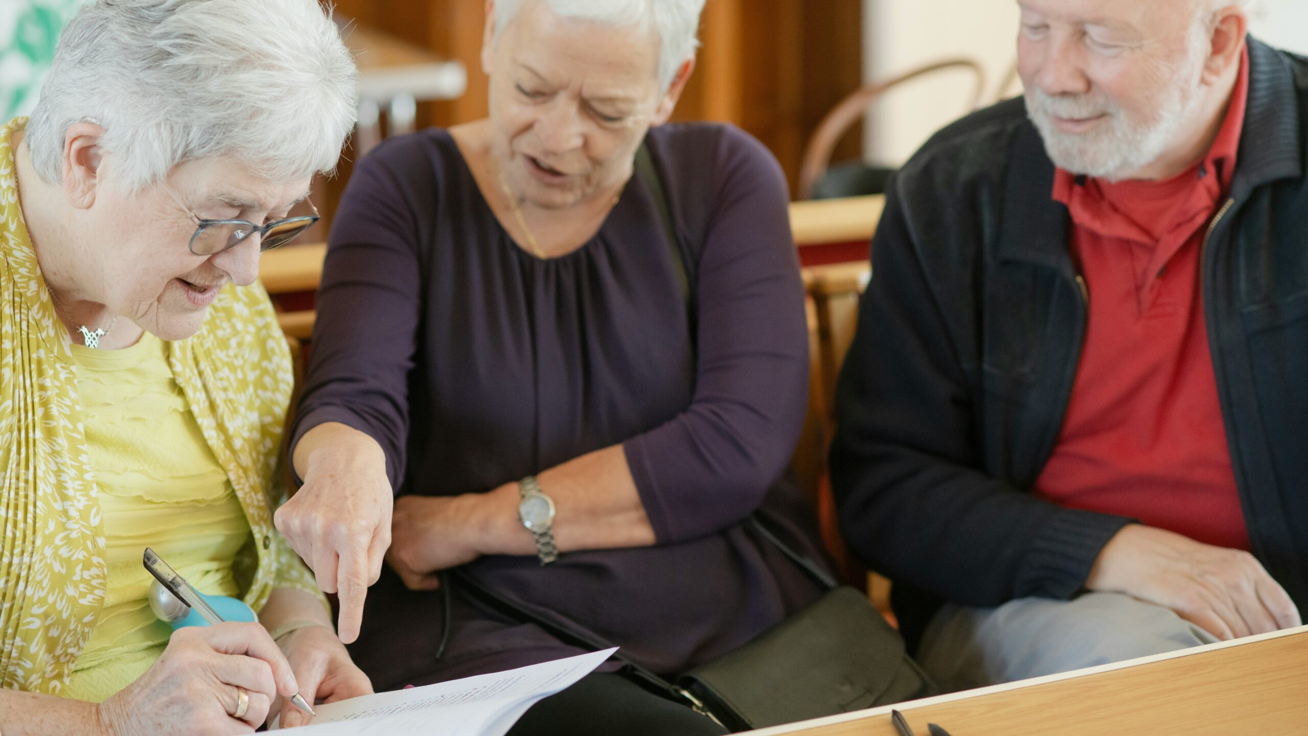 Three older adults are looking at a paper.