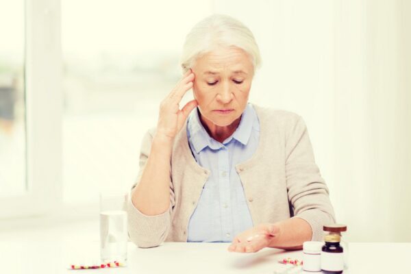 age, medicine, health care and people concept - senior woman with pills and glass of water at home
