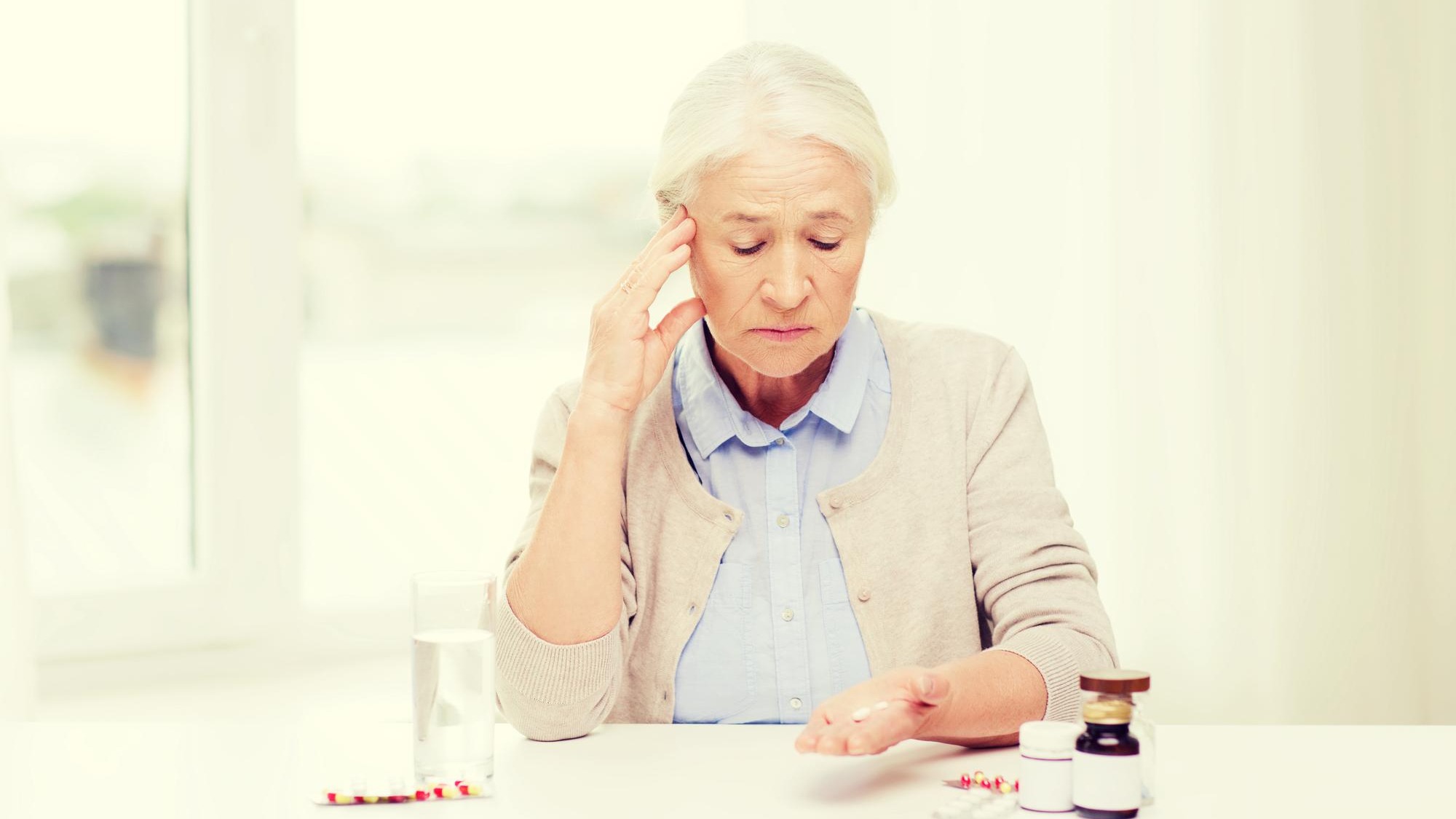 age, medicine, health care and people concept - senior woman with pills and glass of water at home