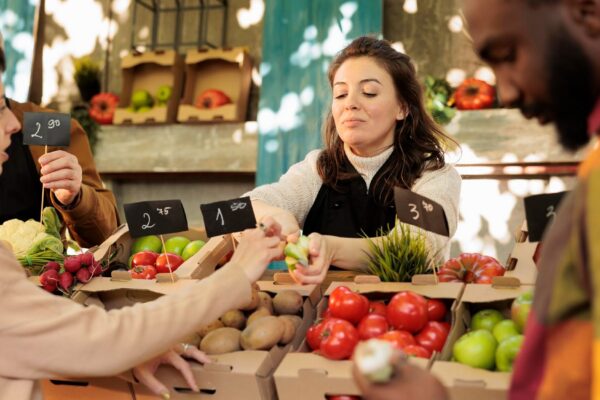 Diverse family couple tasting green apple varieties before buying fresh organic fruits and vegetables at farmers market. Farm produce stand owner offering free samples, bio natural products.