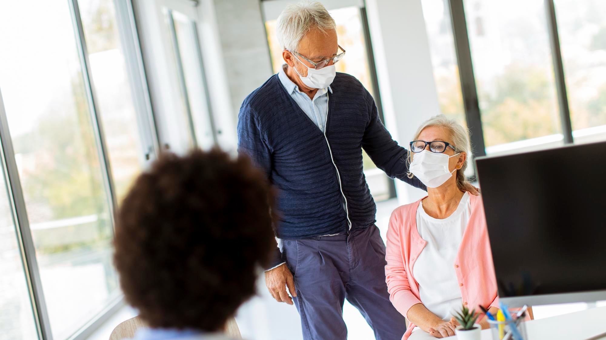 Senior couple with protective facial masks receive news from black female doctor