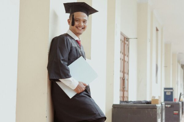 A smiling graduate in cap and gown holds a folder.