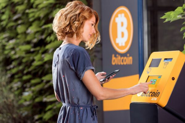 a woman using a cell phone in front of a bitcoin machine