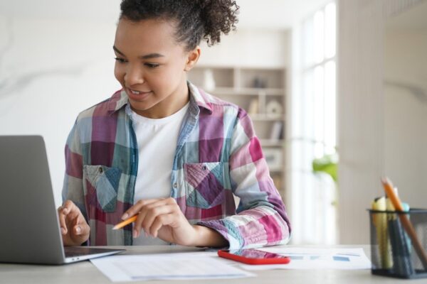 Mixed race teen girl student looking at laptop screen learning online at home Distance education