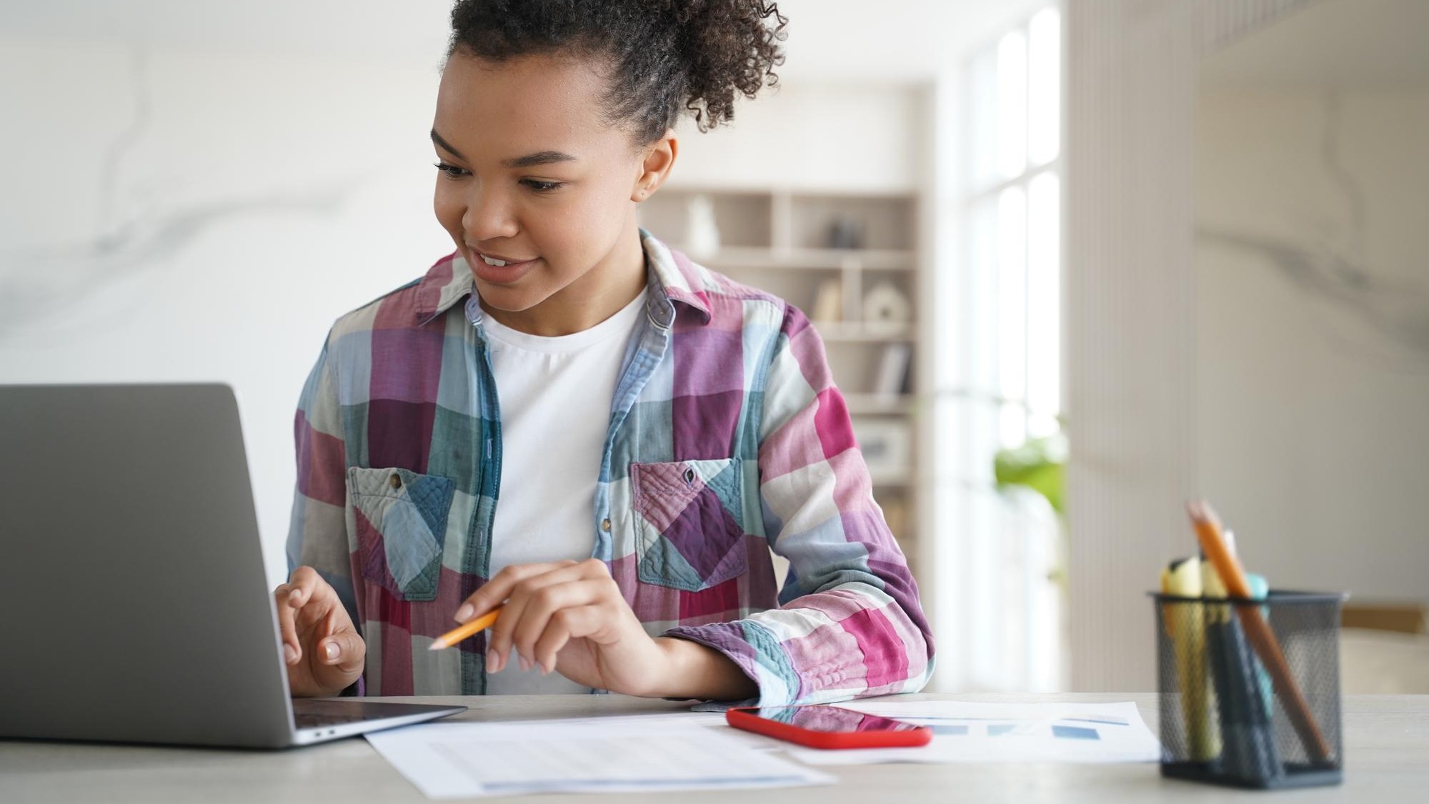 Mixed race teen girl student looking at laptop screen learning online at home Distance education