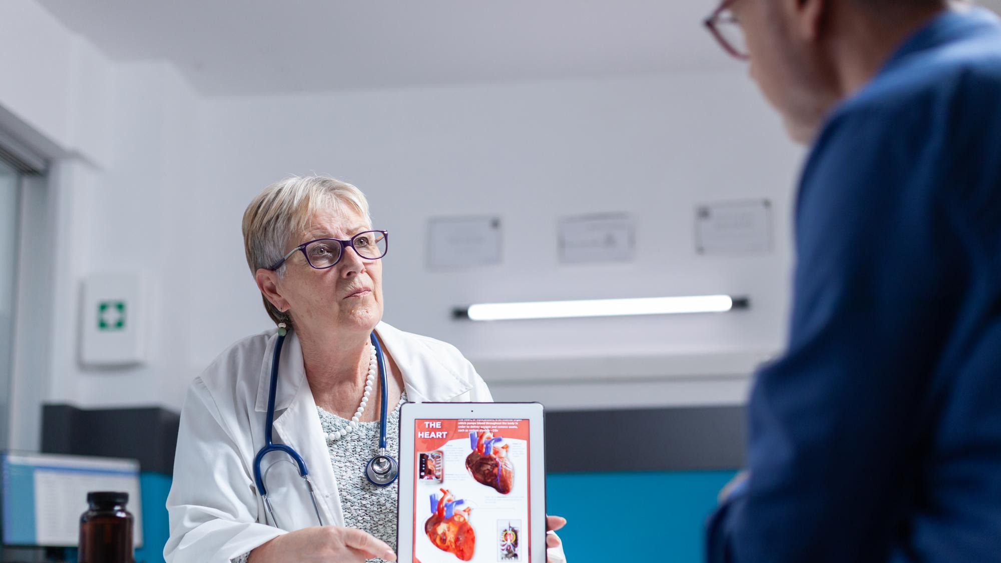 Specialist talking about cardiology diagnosis with image of heart organ on tablet to man. General practitioner showing illustration on cardiovascular system and anatomical structure to patient.