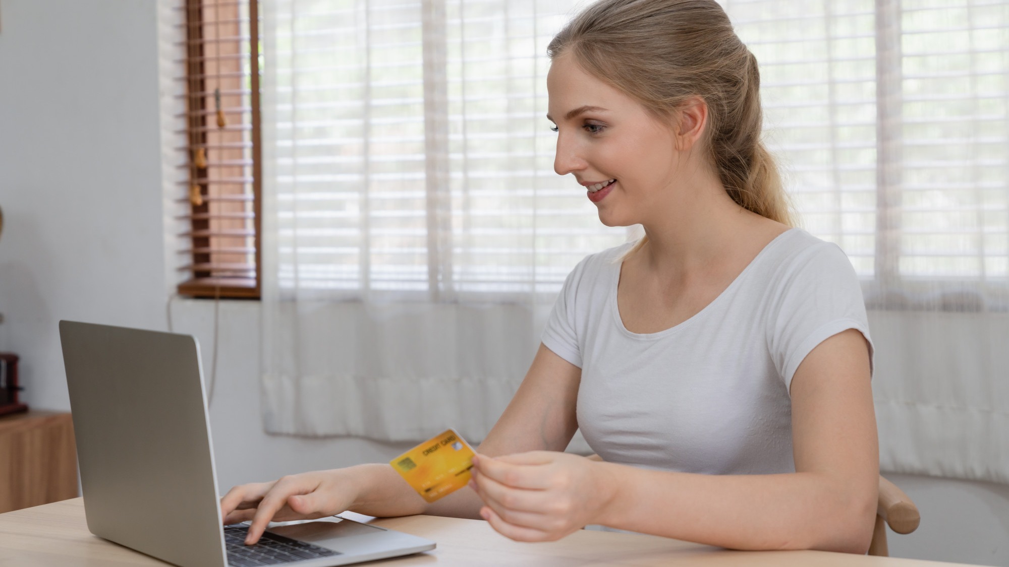 Beautiful young woman using credit card shopping online at home