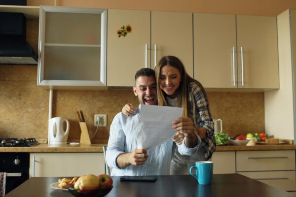 Attractive happy couple receive good news unfolding letter in the kitchen while have breakfast