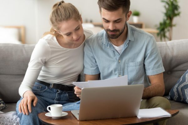 Young serious couple reading financial documents checking bills with laptop
