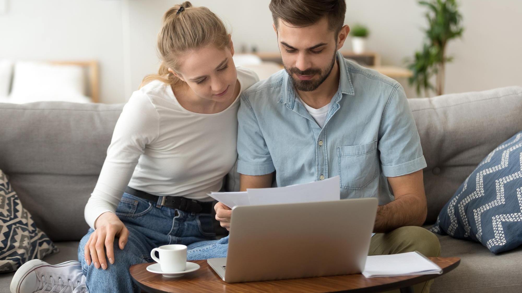 Young serious couple reading financial documents checking bills with laptop
