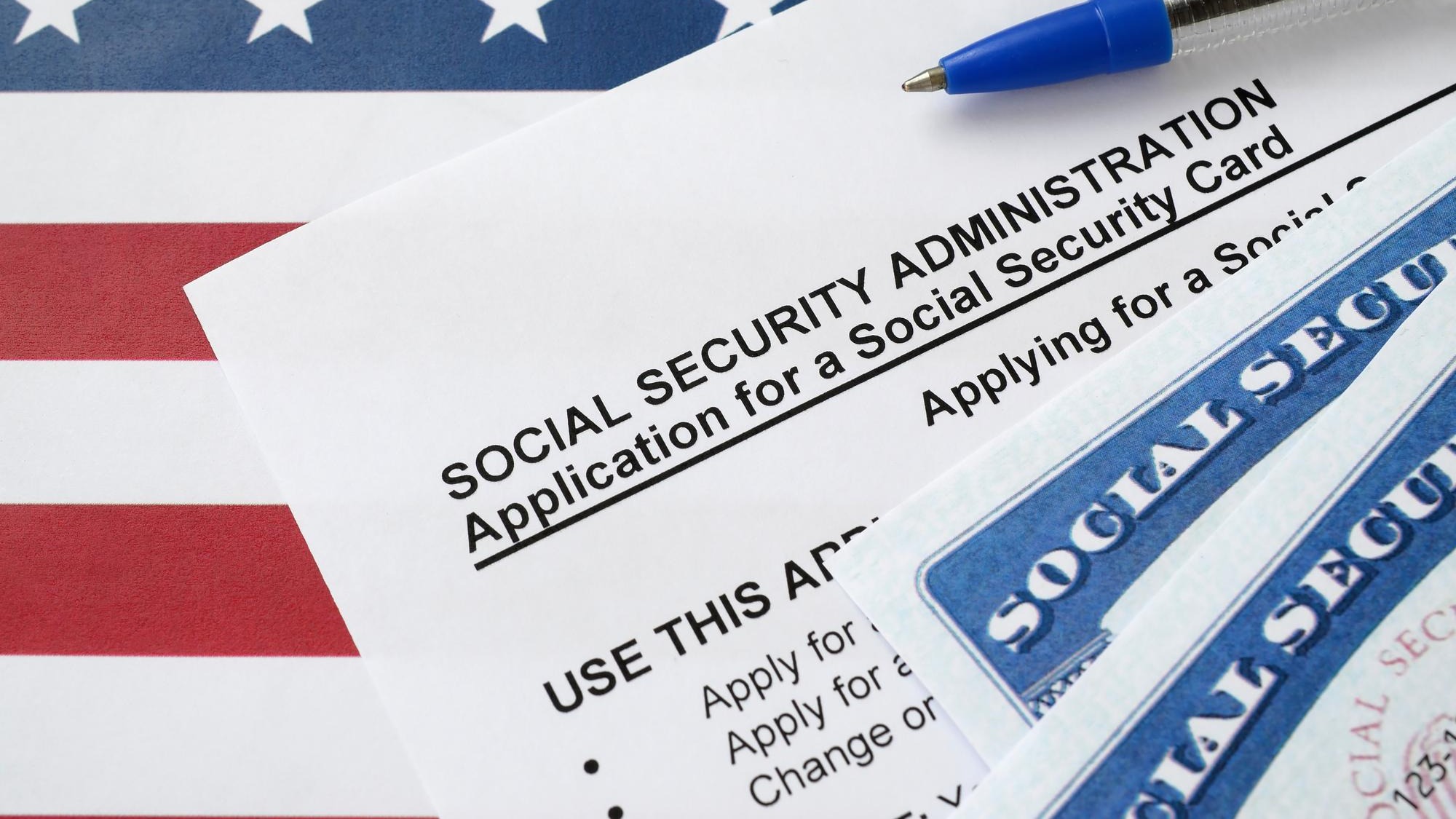 United States social security number cards lies on Application from social security administration with blue pen on US flag