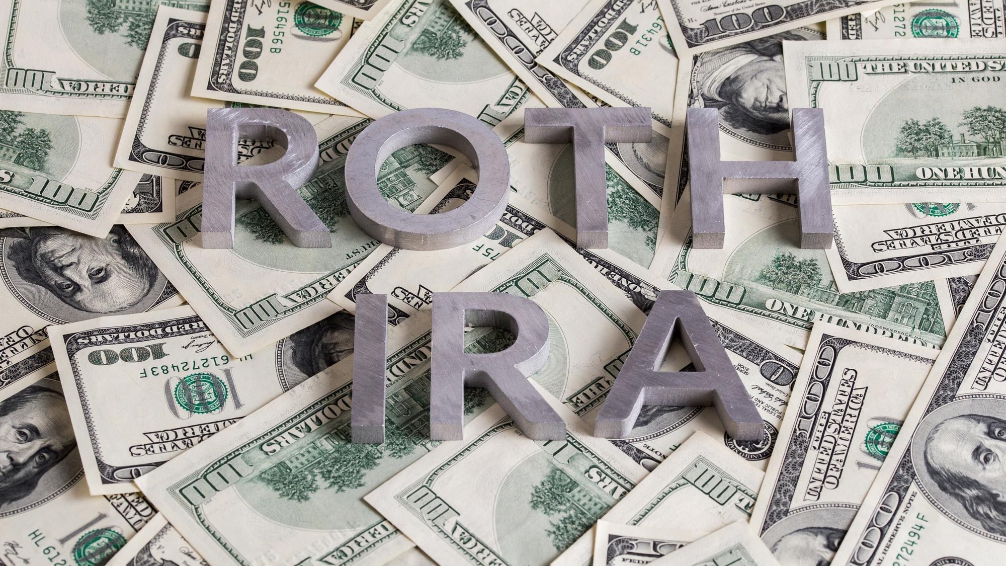 The words ROTH IRA laid with aluminium letters on the US dollar banknotes background with selective focus