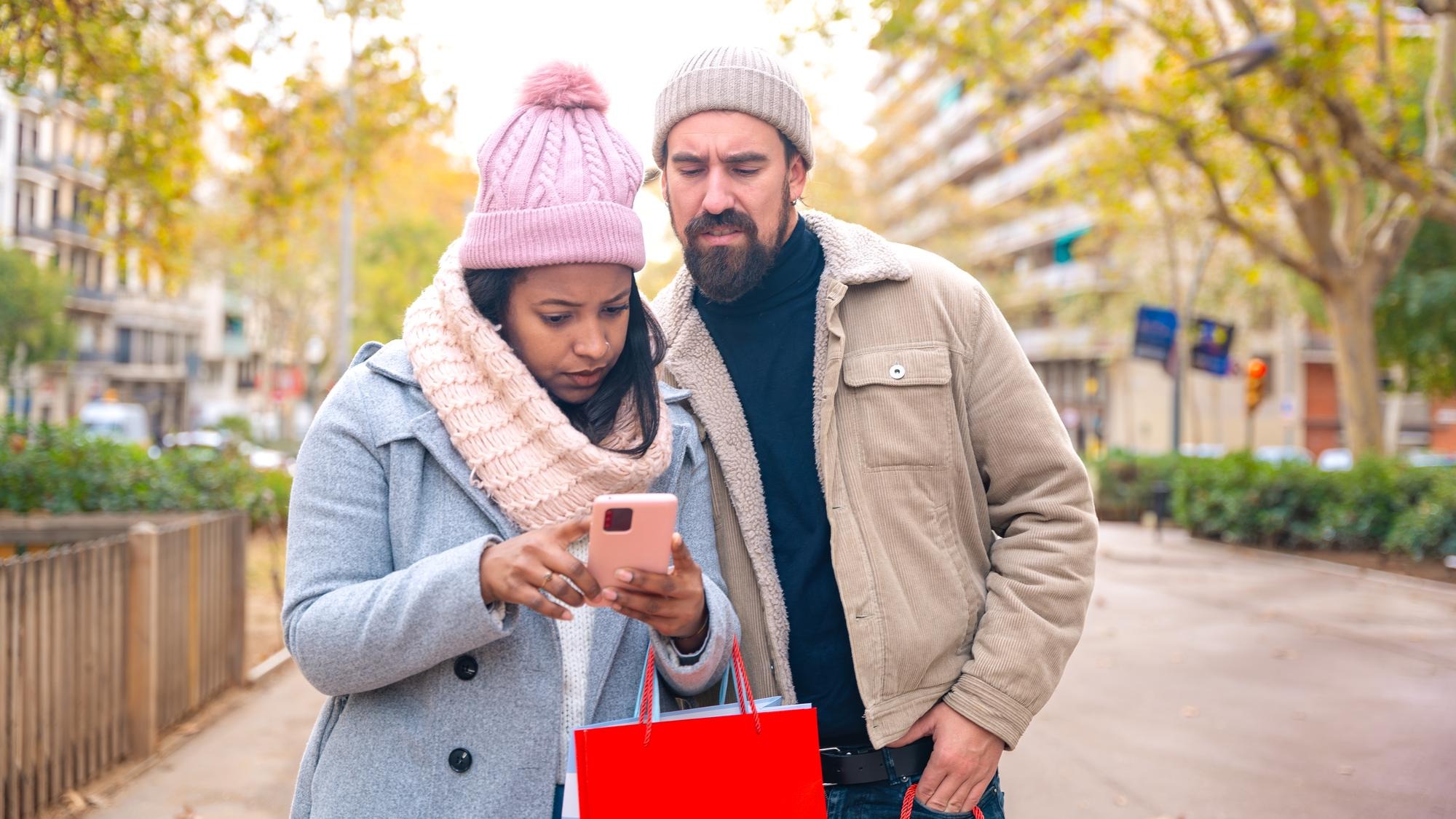 Smiling young multiracial couple holding shopping bags browsing smartphone apps