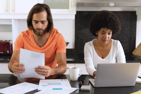 Diverse couple sitting in kitchen using laptop and paying bills. staying at home in isolation during quarantine lockdown.