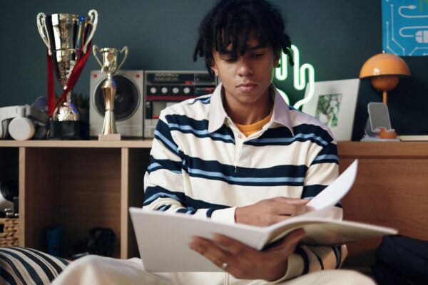 Young adult black man reading book in modern room with trophies displayed