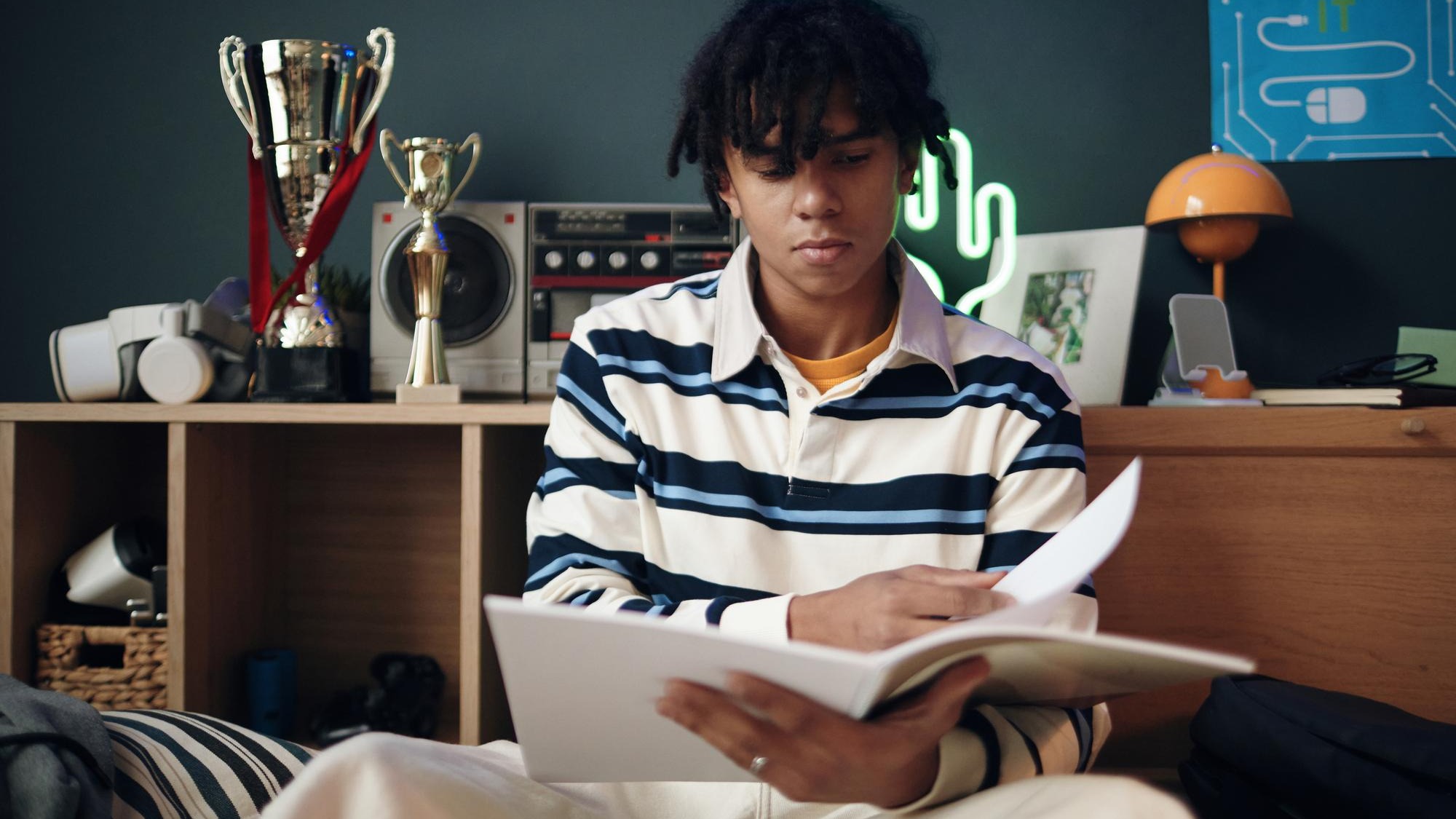 Young adult black man reading book in modern room with trophies displayed