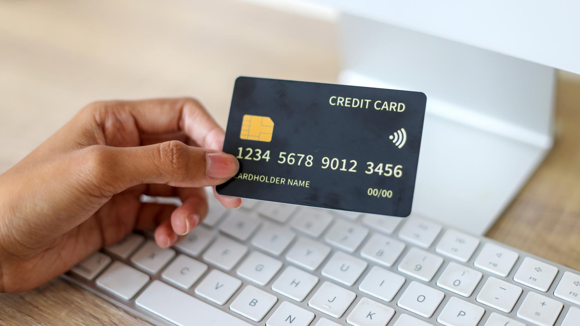 Hand Showing Blank Black Credit Card Mockup Against Keyboard Background