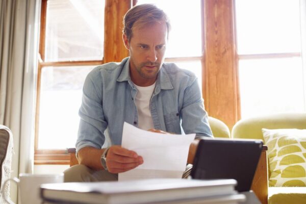 Documents tablet and man in living room planning for debt mortgage or tax payments in home Paperwork digital technology and male person with credit application savings or monthly budget in house