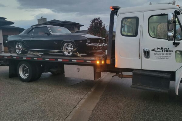 A black classic car loaded onto a tow truck.