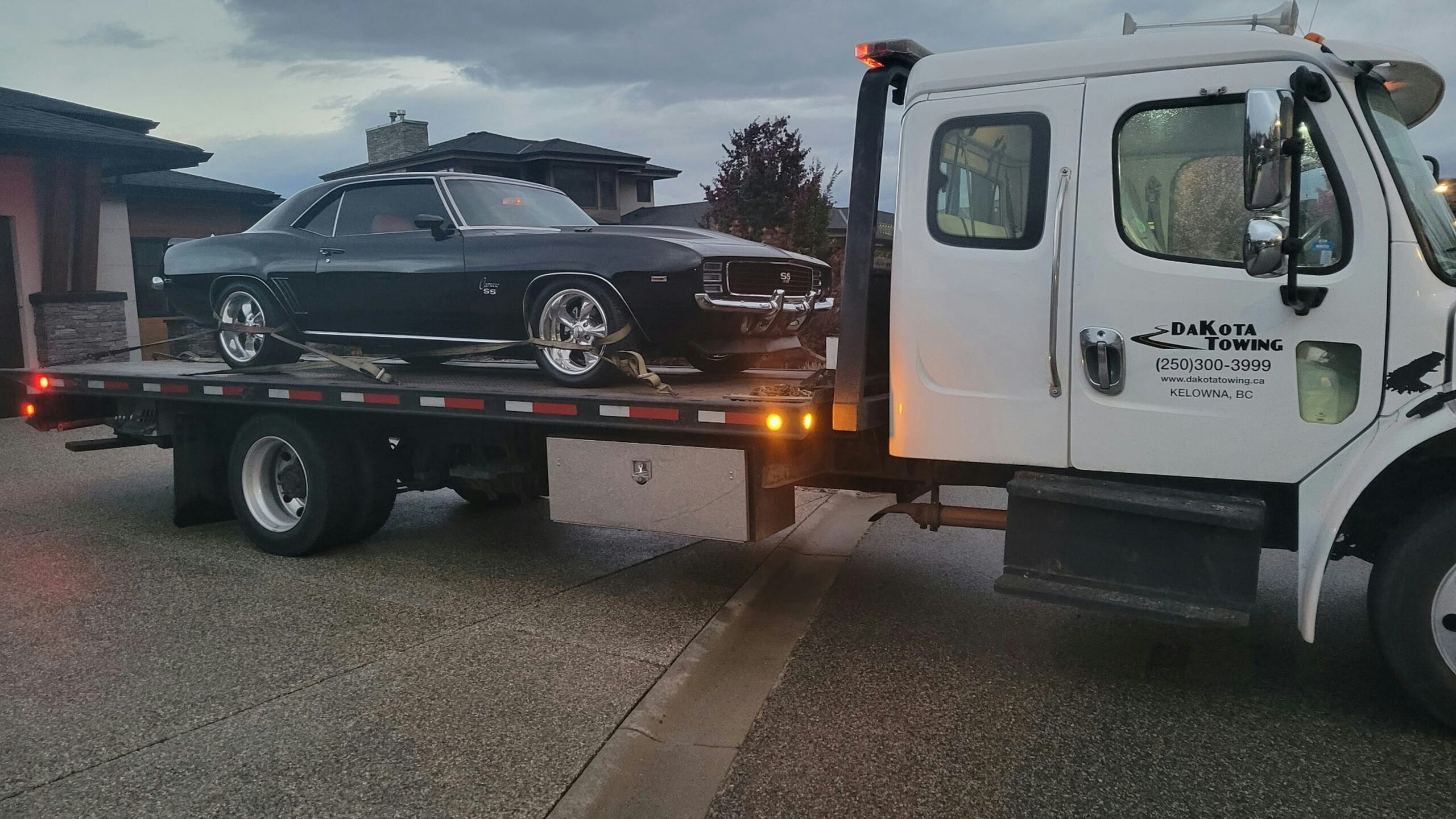 A black classic car loaded onto a tow truck.