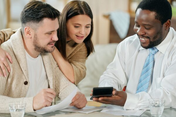 Adult smiling black man with calculating machine showing young couple their interest rate