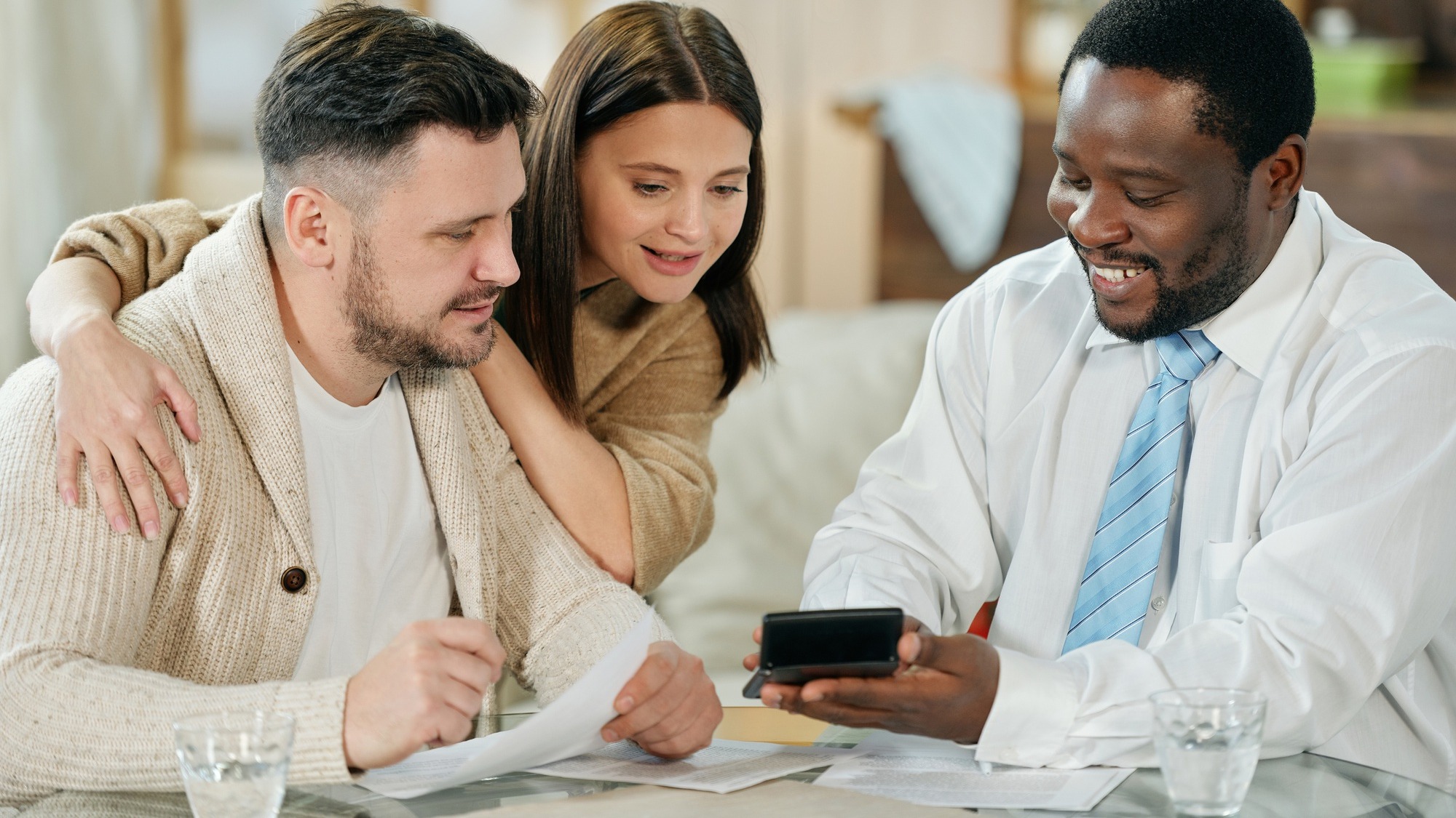 Adult smiling black man with calculating machine showing young couple their interest rate