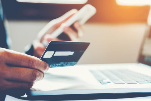 Midsection of man holding credit card while shopping on mobile phone over table