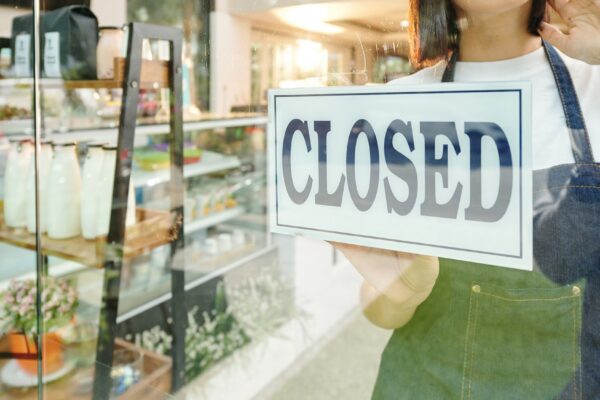 Sad female coffeeshop barista hanging sign on glass wall when closing place at night