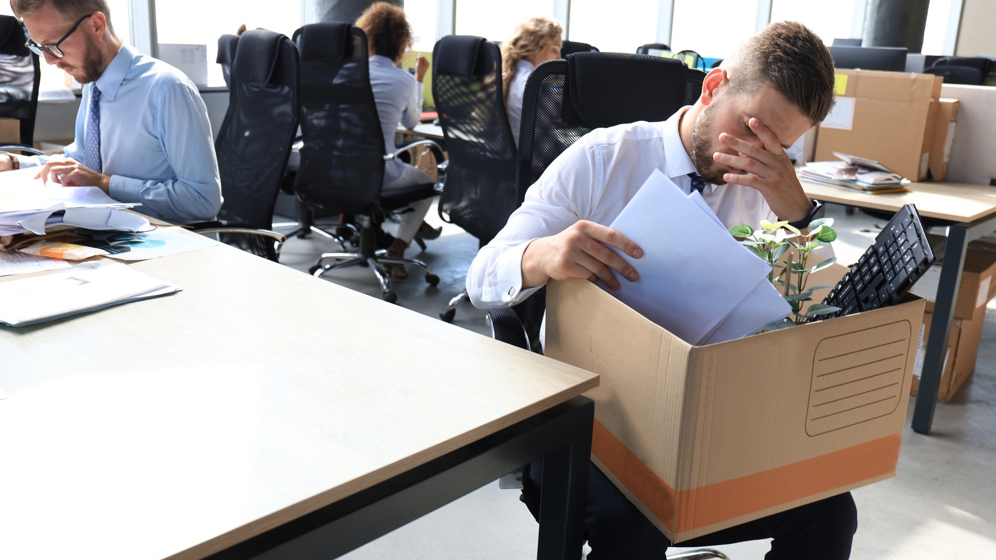 Sad dismissed worker are taking his office supplies with him from office.