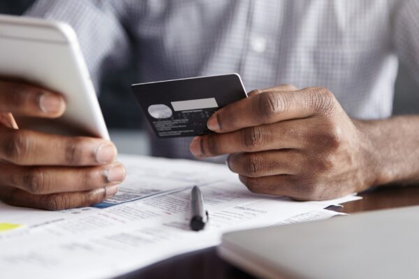 African man in shirt paying for goods on internet using credit card and cell phone