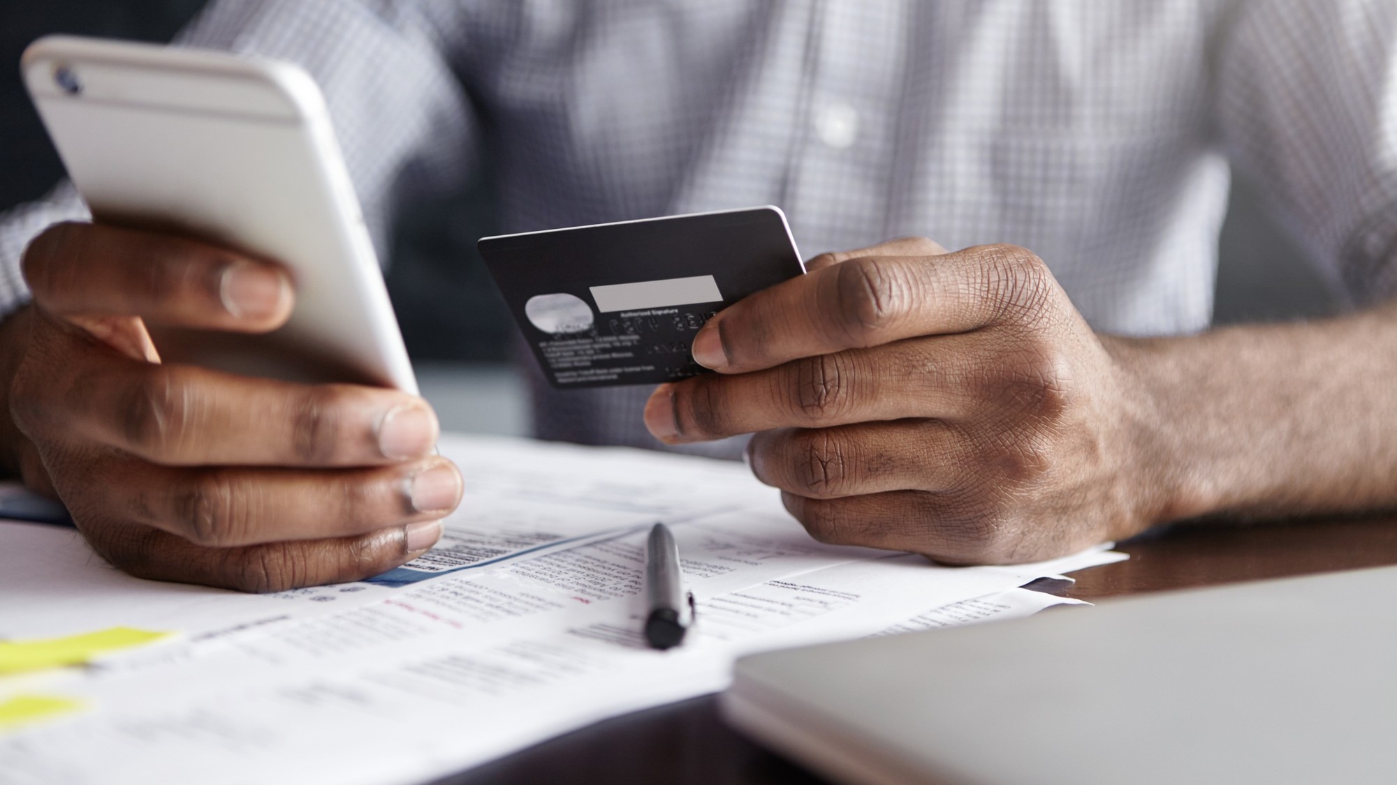 African man in shirt paying for goods on internet using credit card and cell phone