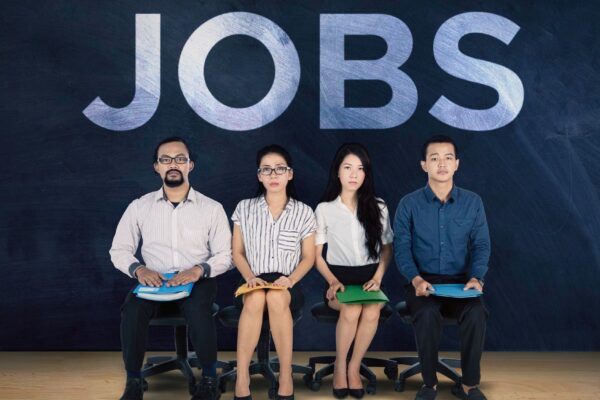 Multicultural young people waiting for a job interview with the text JOBS on a blackboard