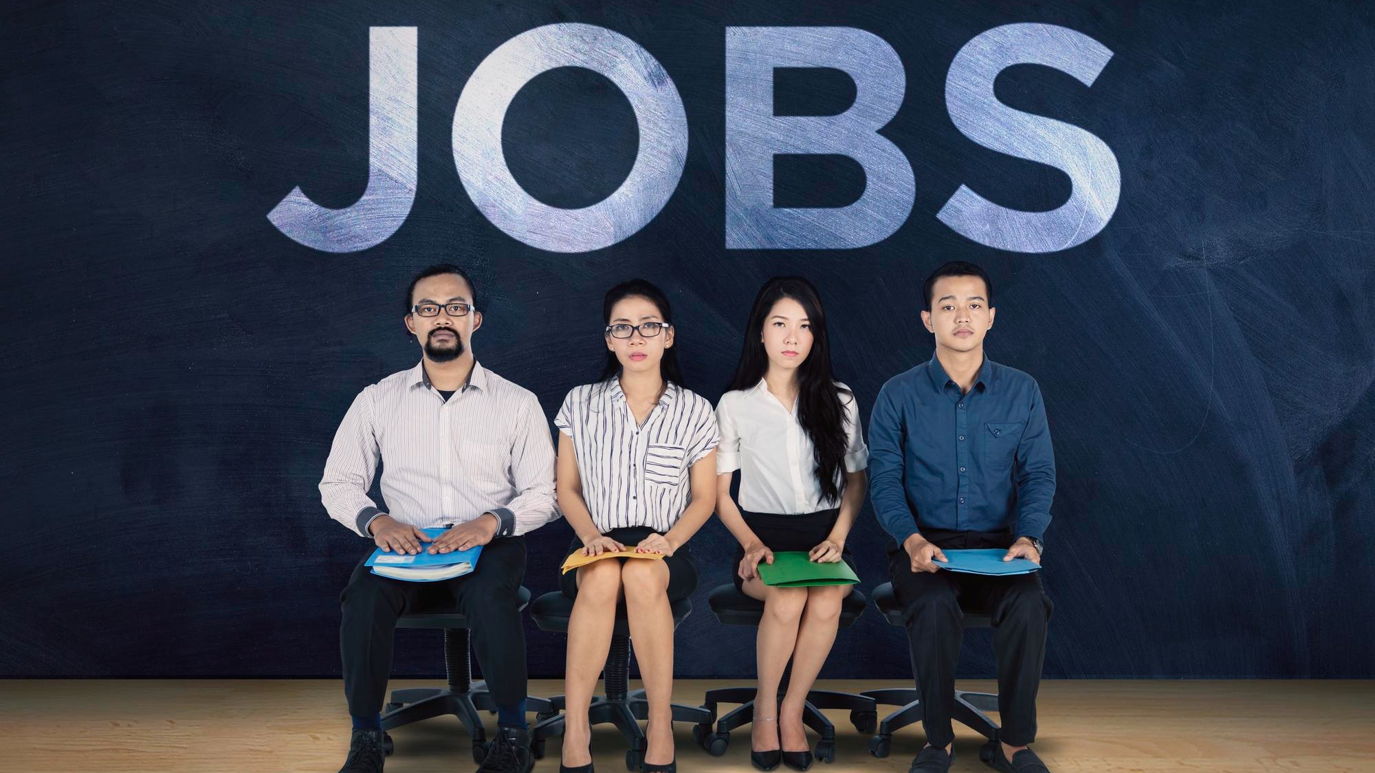 Multicultural young people waiting for a job interview with the text JOBS on a blackboard